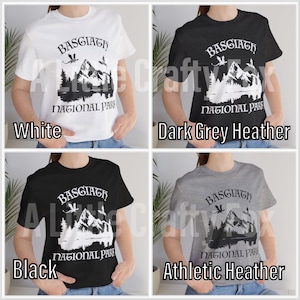 May include: A collection of four t-shirts in white, dark grey heather, black, and athletic heather. Each shirt features the text "BASGIATH NATIONAL PARK" with a mountain and forest graphic. The shirts are short-sleeved.