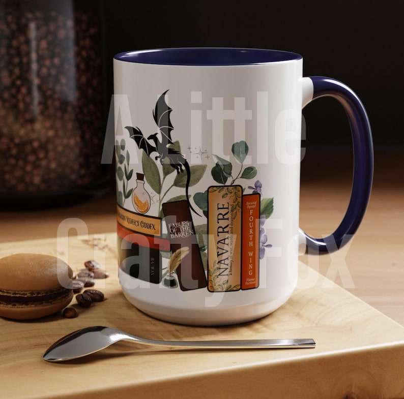 May include: White ceramic mug with a blue rim and handle. The mug features a black dragon, green leaves, and a stack of books with titles like "Navarre" and "Fourth Wing".