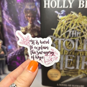 May include: A white sticker with a pink and purple illustration of a sword and a heart. The sticker has the text "It is hard to explain the savagery of hope".