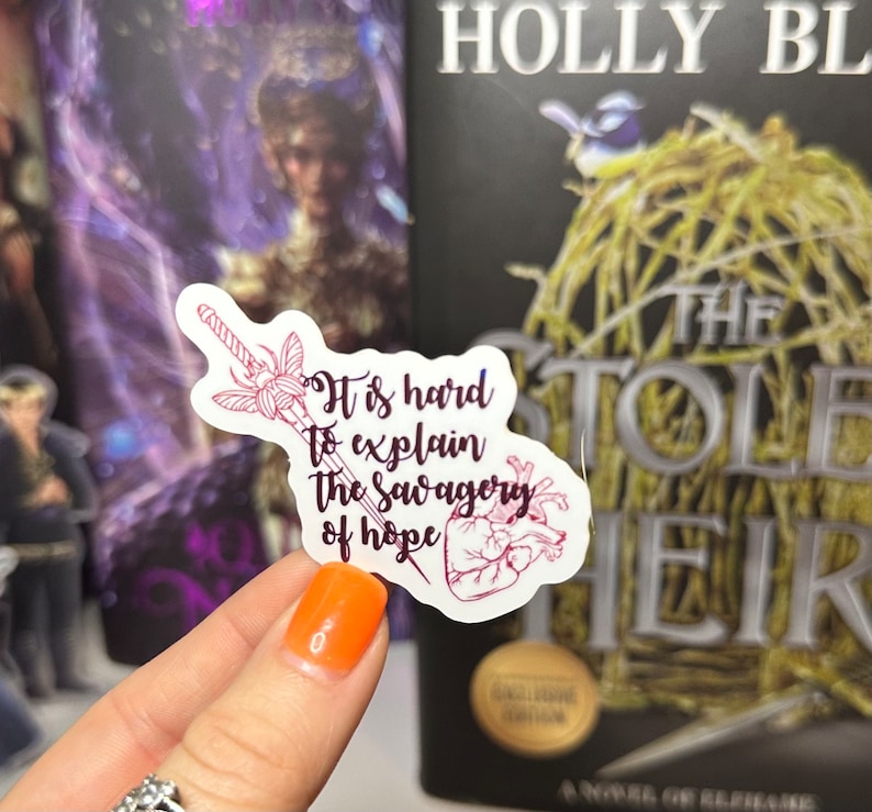 May include: A white sticker with a pink and purple illustration of a sword and a heart. The sticker has the text "It is hard to explain the savagery of hope".