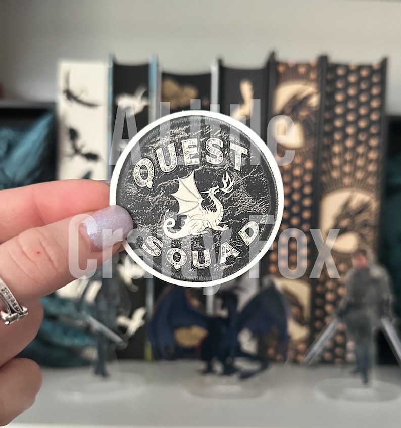 May include: A round sticker with a black background and white text and a dragon design. The sticker says "Quest Squad" with a dragon in the center.