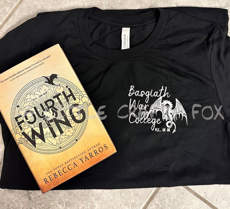 Pu&ograve; includere: Una maglietta nera con la scritta "Basgiath War College" e un disegno di drago. Accanto alla maglietta c'&egrave; un libro intitolato "Fourth Wing" di Rebecca Yarros, con un design circolare e le parole "Fly or Die".