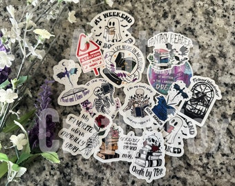 Puede incluir: Una colección de 12 pegatinas de temática de libros con varios diseños, incluyendo un fantasma leyendo un libro, un esqueleto sosteniendo un libro, un dragón y una pila de libros con el texto "Death by TBR".