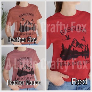 May include: Three t-shirts in heather clay, heather mauve, and red. Each shirt features a black graphic of mountains, trees, and birds, with the text "BASGIATH NATIONAL PARK". The shirts are short-sleeved.