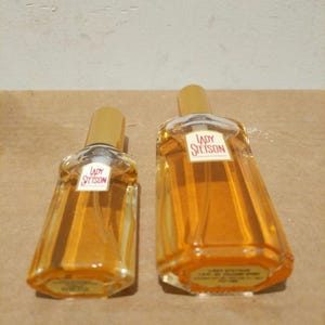 May include: Two glass bottles of perfume with gold caps. The bottles are clear and contain a yellow liquid. The bottles have a label that says "Lady Stetson" in red letters.