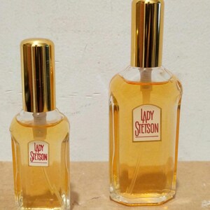 May include: Two glass bottles of Lady Stetson perfume. The bottles are clear glass with gold caps and a rectangular shape. The larger bottle is about 4 inches tall and the smaller bottle is about 2 inches tall.