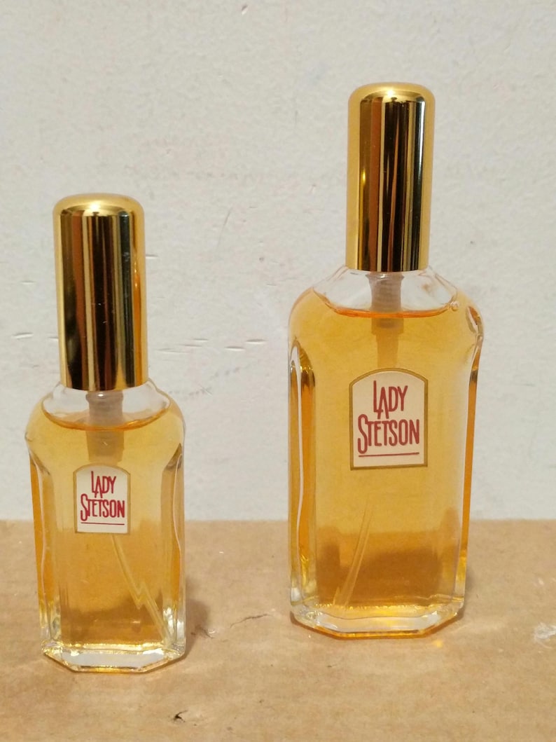 May include: Two glass bottles of Lady Stetson perfume. The bottles are clear glass with gold caps and a rectangular shape. The larger bottle is about 4 inches tall and the smaller bottle is about 2 inches tall.