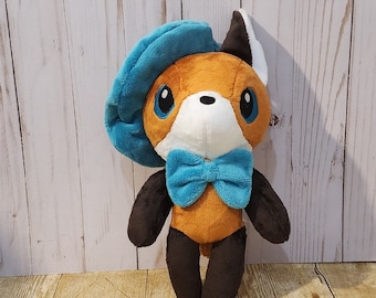 May include: A plush fox toy with orange fur, black paws, and a white face. It wears a teal beret and bow tie. The fox has large blue eyes and is posed against a light wood background.