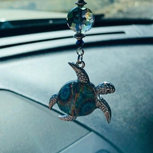 Könnte beinhalten: Ein blauer und silberner Auto-Anhänger mit einer Perlenkette, einer Kristallperle und einer silbernen Schildkröte mit einem blau-grünen gemusterten Panzer.
