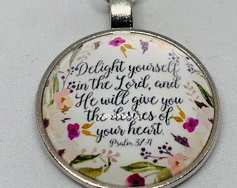 May include: A round pendant with a floral design and the text "Delight yourself in the Lord, and He will give you the desires of your heart. Psalm 37:4." The pendant is silver-toned and has a beaded top.