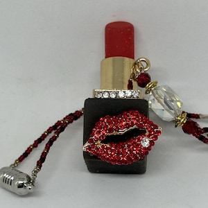 May include: A red lipstick charm with a rhinestone-encrusted base and a red lip charm. The charm is attached to a beaded chain with a silver clasp.
