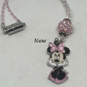 May include: A pink and white Minnie Mouse charm hangs from a silver chain with a pink and clear crystal bead. The chain has a magnetic clasp.