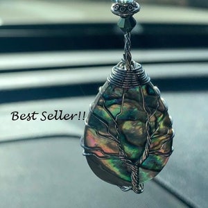 May include: A car charm featuring a teardrop-shaped abalone shell with a silver wire tree design, accented with a crystal bead and silver chain.