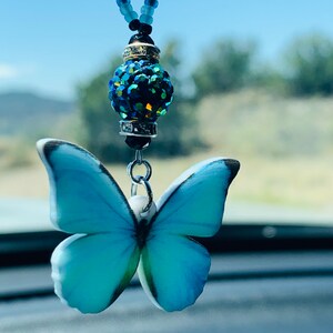 May include: A blue butterfly charm with a crystal bead hanging from a beaded chain. The charm is a car accessory.