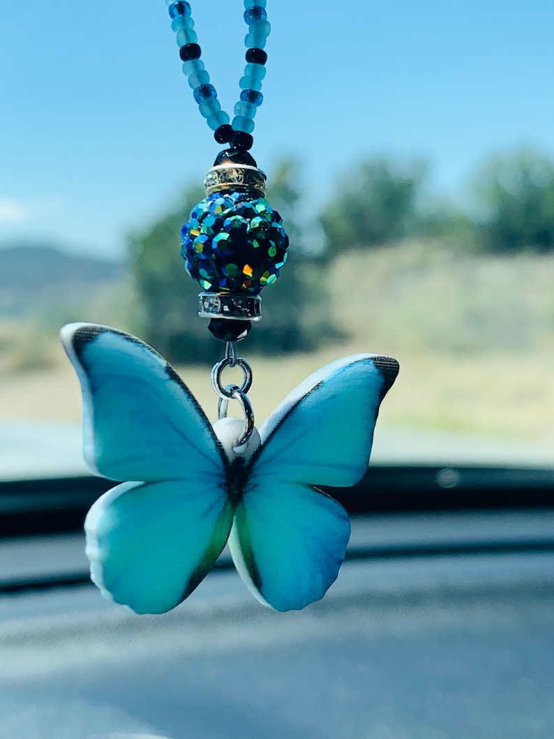 May include: A blue butterfly charm with a crystal bead hanging from a beaded chain. The charm is a car accessory.
