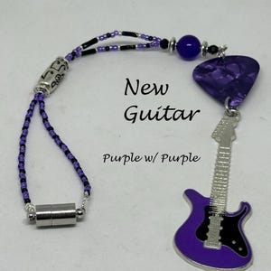 May include: A purple guitar charm with a black pickguard and silver strings. The charm is attached to a purple and black beaded necklace with a silver magnetic clasp. The charm is labeled "New Guitar Purple w/ Purple".