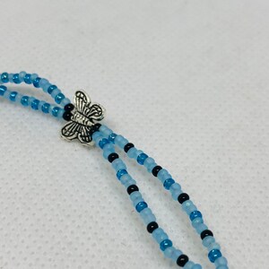 May include: A beaded necklace with a silver butterfly charm. The necklace is made with light blue and black beads.