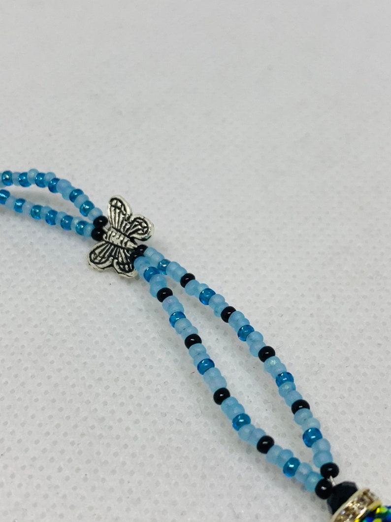 May include: A beaded necklace with a silver butterfly charm. The necklace is made with light blue and black beads.