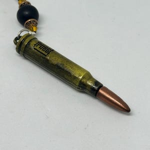 May include: A gold-colored bullet pendant necklace with a black bead and brown and gold beads on the chain. The bullet has the word "PUBG" engraved on the side.