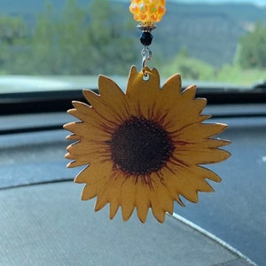 May include: A yellow sunflower car charm with a black center and a sparkly iridescent bead hanging from a silver chain.