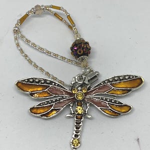 May include: A silver dragonfly charm with orange and pink enamel and yellow rhinestone accents. The charm is attached to a beaded chain with a crystal bead.