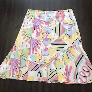 May include: A white skirt with a colorful geometric pattern. The skirt has a ruffled hem and is made of a lightweight fabric.