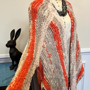 May include: A long, orange and gray striped cardigan with a fringed hem. The cardigan is made of a soft, fuzzy material.