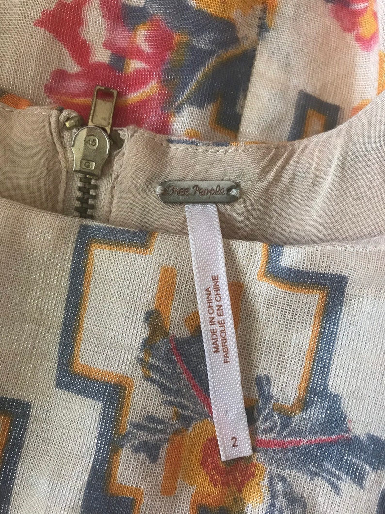 May include: Close-up of a cream-colored dress with a floral and geometric pattern in shades of red, yellow, and blue. The dress features a metal zipper and a tag that reads "Free People" and "Made in China". Size 2.