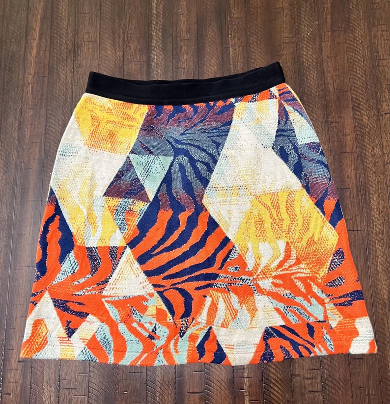 Puede incluir: Una falda de colores con estampado geom&eacute;trico y cintura negra. La falda est&aacute; hecha de tejido tejido y presenta una variedad de colores, incluyendo naranja, amarillo, azul y blanco.
