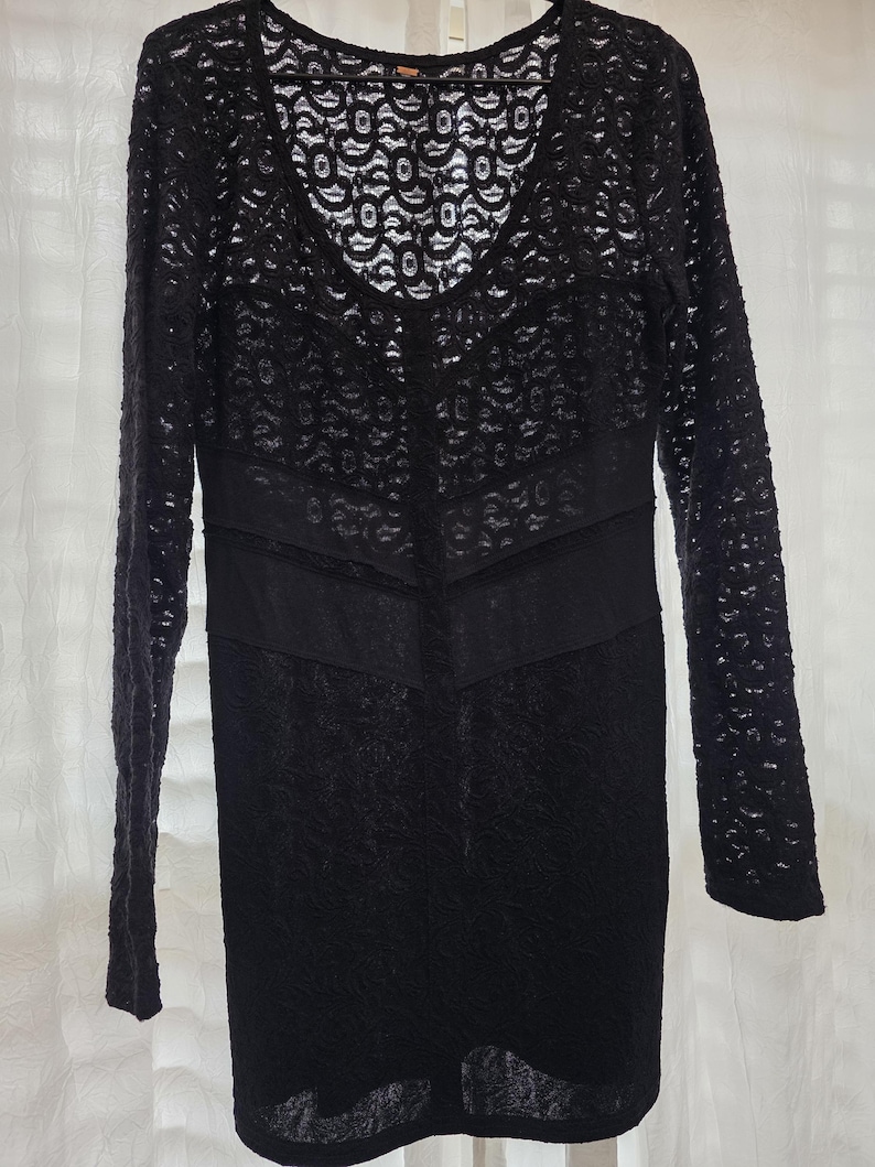 May include: Black lace dress with long sleeves and a V-neckline. The dress features a fitted bodice and a straight skirt. The lace pattern is intricate and detailed, creating a delicate and elegant look. The dress is suitable for special occasions.