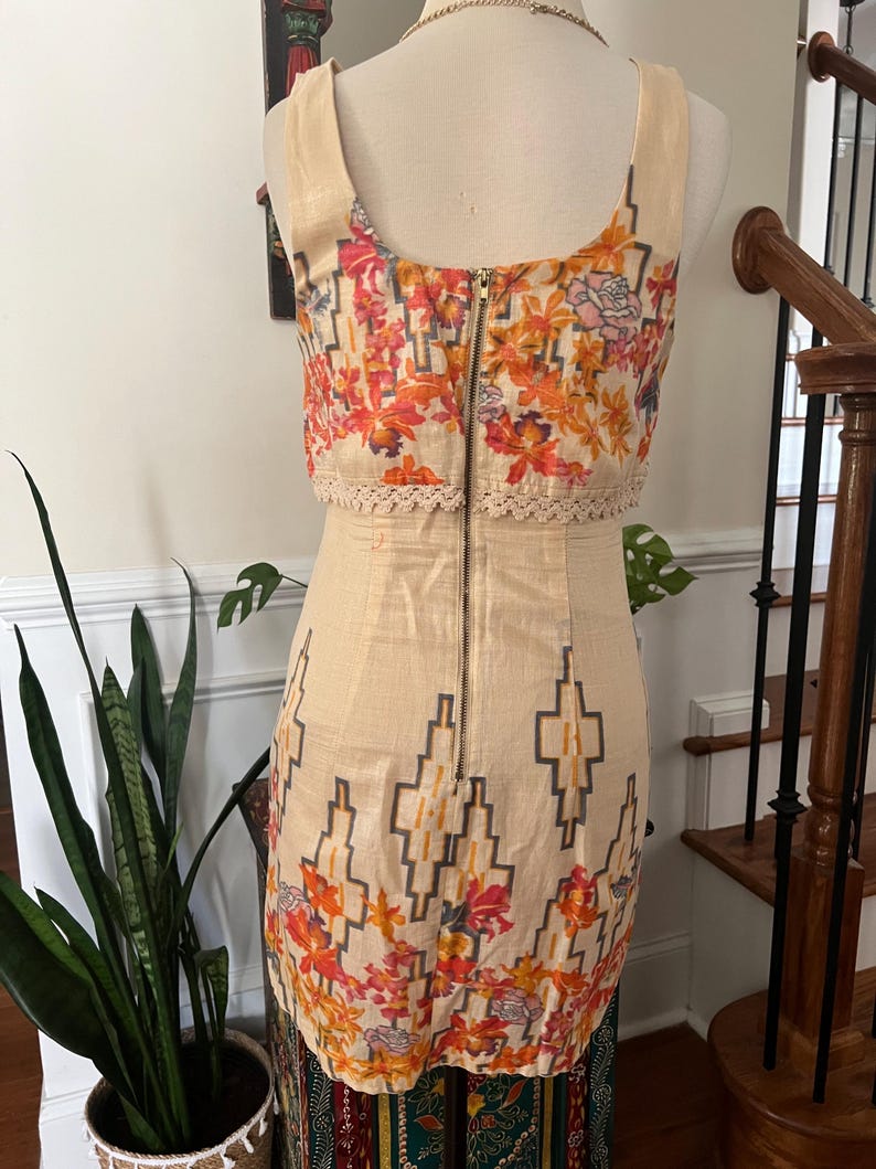 May include: A beige sleeveless dress with a floral and geometric pattern. The top section features a colorful floral print with orange, pink, and yellow flowers. The dress has a zipper down the back and a decorative lace trim.