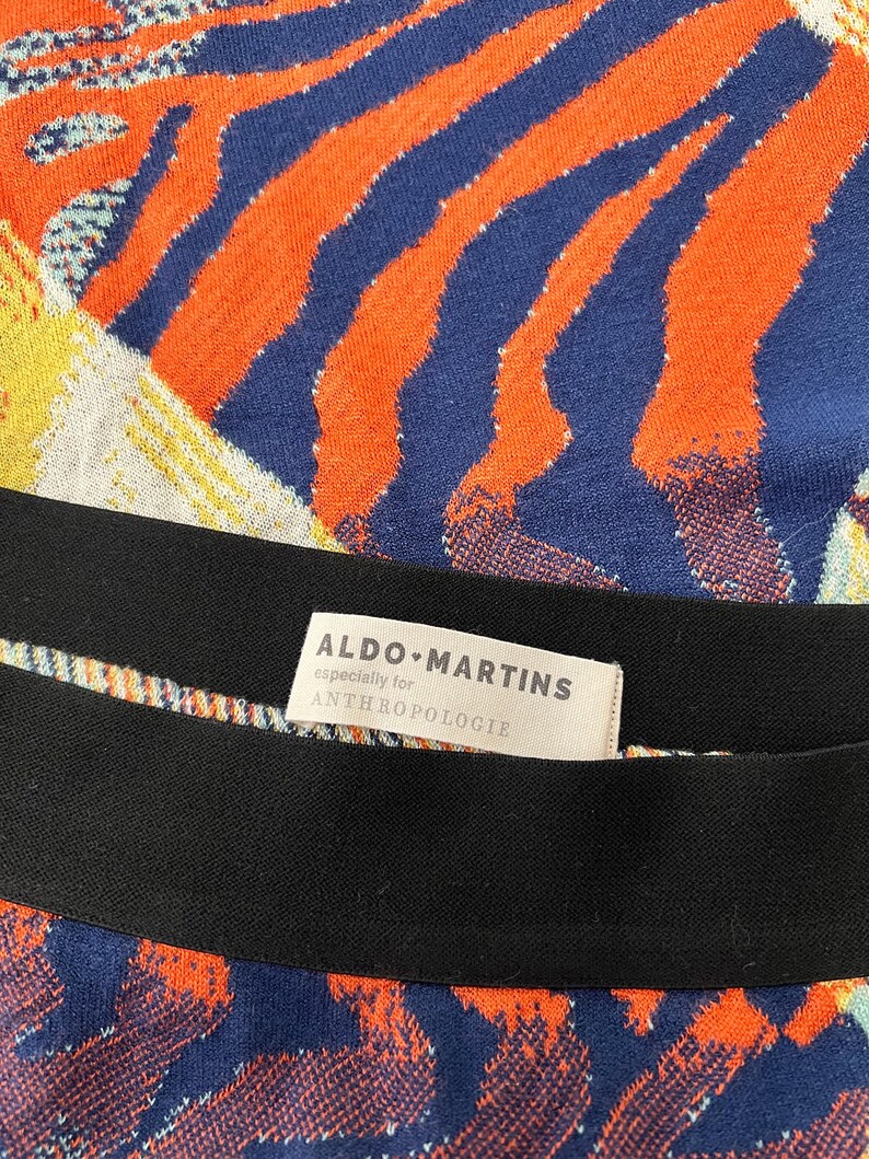 Puede incluir: Una tela de rayas blancas y negras con un patr&oacute;n abstracto azul y naranja. La tela tiene una etiqueta que dice "ALDO MARTINS especially for ANTHROPOLOGIE".