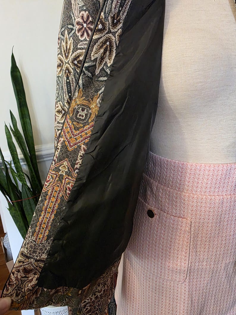 May include: A patterned jacket with a black interior lining. The jacket features a detailed design with brown, gold, and cream colors. The lining is black. The jacket is paired with a pink skirt.