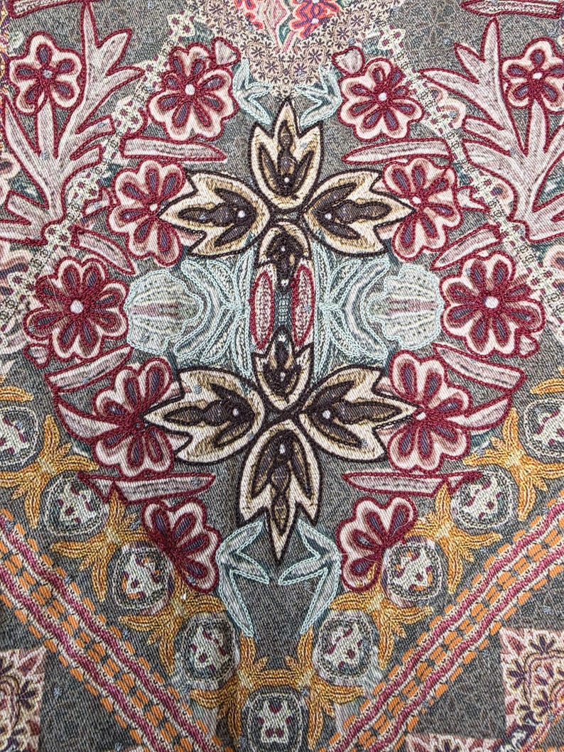 May include: Close-up of a textile with an intricate floral pattern. The design features burgundy, gold, and light blue embroidered flowers and geometric shapes on a gray background. The overall aesthetic is ornate and detailed.