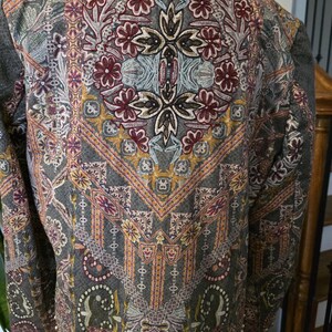 May include: A gray jacket with an intricate floral and geometric pattern in burgundy, gold, and teal. The jacket has a round neckline and is embellished with small, gold-colored studs along the bottom hem.