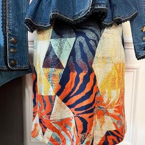 Puede incluir: Una falda colorida con un estampado geom&eacute;trico y de animales. La falda est&aacute; hecha de una tela suave y tejida y tiene una silueta recta. La falda es una mezcla vibrante de naranja, azul, amarillo y blanco.