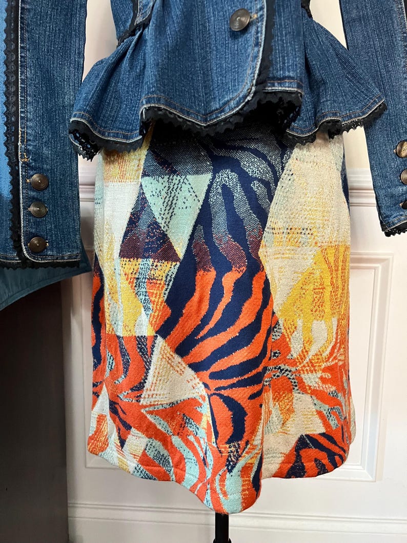 Puede incluir: Una falda colorida con un estampado geom&eacute;trico y de animales. La falda est&aacute; hecha de una tela suave y tejida y tiene una silueta recta. La falda es una mezcla vibrante de naranja, azul, amarillo y blanco.