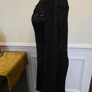 May include: A black dress with lace sleeves and bodice detail. The dress has a fitted silhouette and a scoop neckline. The sleeves are long and made of a delicate lace fabric. The bodice also features lace detailing, adding a touch of elegance to the garment.