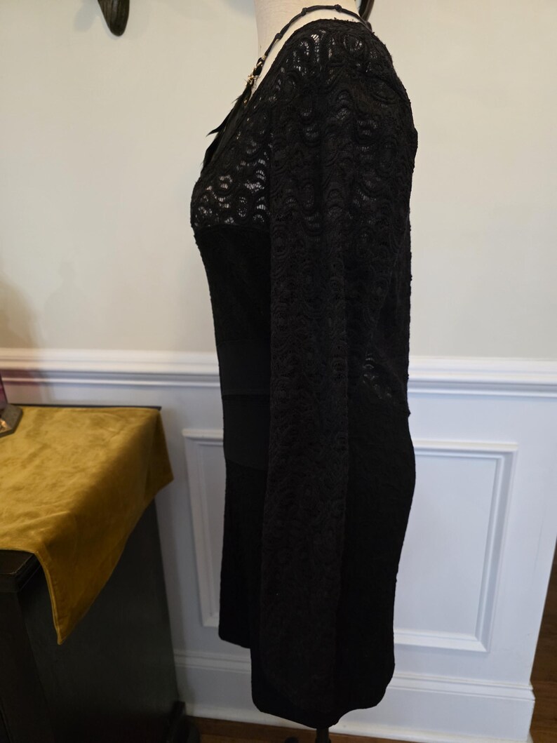 May include: A black dress with lace sleeves and bodice detail. The dress has a fitted silhouette and a scoop neckline. The sleeves are long and made of a delicate lace fabric. The bodice also features lace detailing, adding a touch of elegance to the garment.