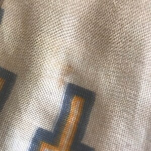 May include: Close-up of a beige fabric with a geometric pattern in shades of gray and yellow. The fabric has a textured, woven appearance.