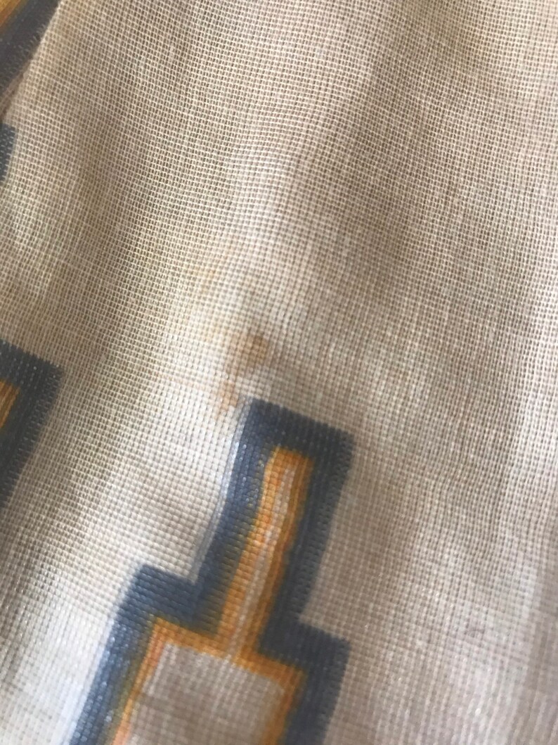 May include: Close-up of a beige fabric with a geometric pattern in shades of gray and yellow. The fabric has a textured, woven appearance.