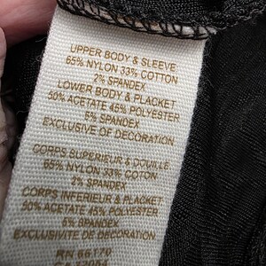 May include: A close-up of a clothing tag with text detailing the fabric composition. The tag lists the materials as nylon, cotton, acetate, polyester, and spandex. The tag also includes French translations of the fabric details.