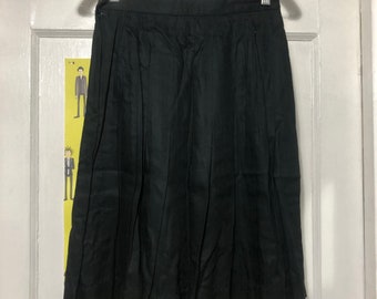 May include: A black pleated skirt hanging on a clear plastic hanger. The skirt is made of a smooth fabric and has a classic, knee-length design. The skirt is hanging on a white door.