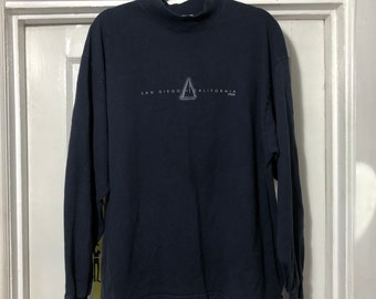 Könnte beinhalten: Ein dunkelblaues Langarmshirt mit Stehkragen. Das Shirt hat eine weiße Grafik eines Segelboots mit dem aufgedruckten Text "San Diego California".