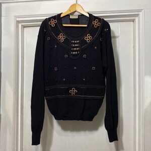 May include: Black sweater with a high neckline and intricate gold and brown beading. The sweater has a geometric pattern and is made of a soft, knit fabric.