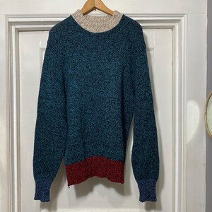 May include: A teal blue sweater with a red and white trim. The sweater has a textured knit and a mock neck.