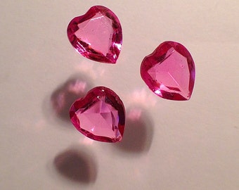 May include: Three pink heart-shaped glass gems. The gems are faceted and have a shiny finish.