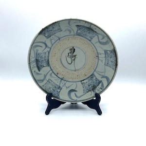 Peut inclure: Une assiette en céramique bleue et blanche avec un motif décoratif. L'assiette est de forme circulaire et décorée d'un motif bleu et blanc. L'assiette est sur un support noir.