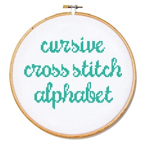 May include: A cross-stitch embroidery hoop with the words "cursive cross stitch alphabet" stitched in teal thread on white fabric. The wooden hoop is round and has a brass clasp.
