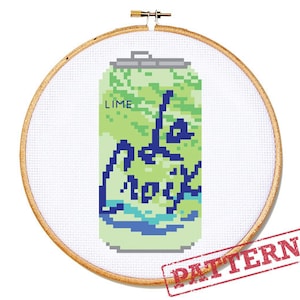 May include: Cross-stitch pattern of a lime-flavored La Croix can, displayed in a wooden embroidery hoop. The can design features pixelated shades of green, blue, and white, with the word "LIME" at the top. The La Croix logo is visible. A red "PATTERN" stamp is in the lower right.